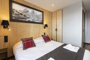 A bedroom with a large bed, two plaid pillows, a framed picture on the wall, and a wardrobe. - Apartment in Le Corbier Near Ski Slopes (Villarembert)