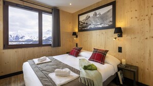 Une chambre d’hôtel avec un grand lit, deux oreillers, une table de chevet avec une lampe, un tableau encadré au mur et une fenêtre donnant sur des montagnes enneigées.