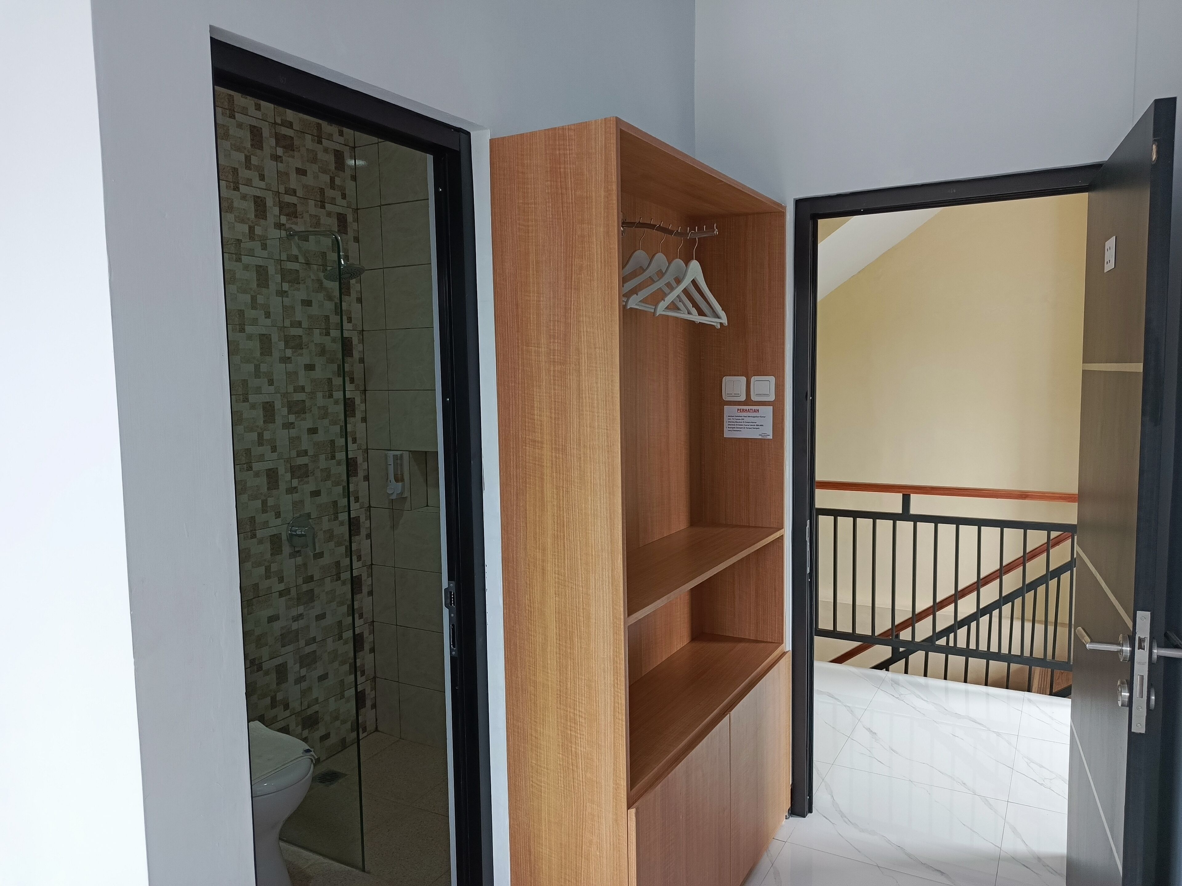 Una habitación con un armario de madera, una zona de ducha con azulejos y una escalera con barandilla negra.