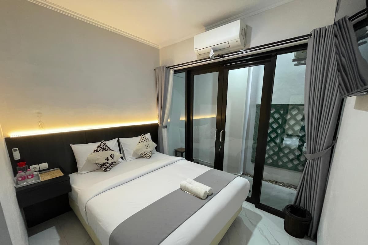 Une chambre d’hôtel moderne avec un lit soigneusement fait, une table de chevet avec une lampe et une porte-fenêtre coulissante donnant sur un balcon.
