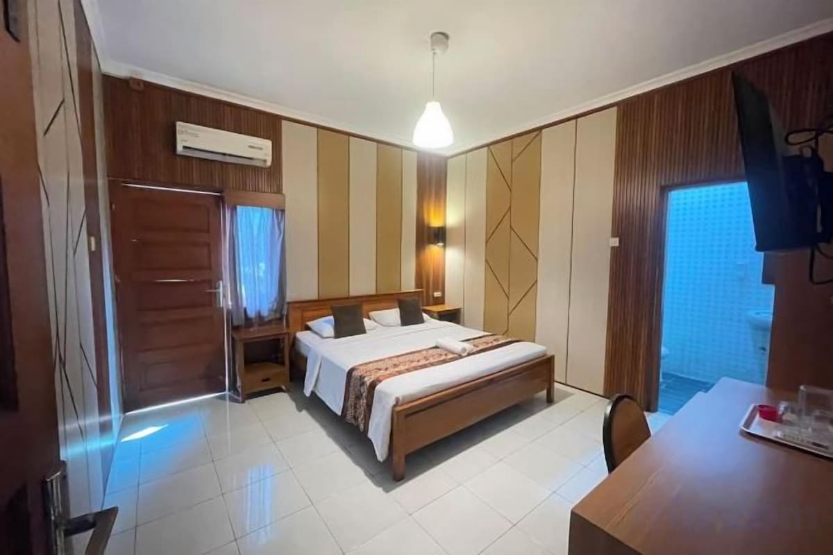 A bedroom with a bed, bedside table, and a view of the outside.