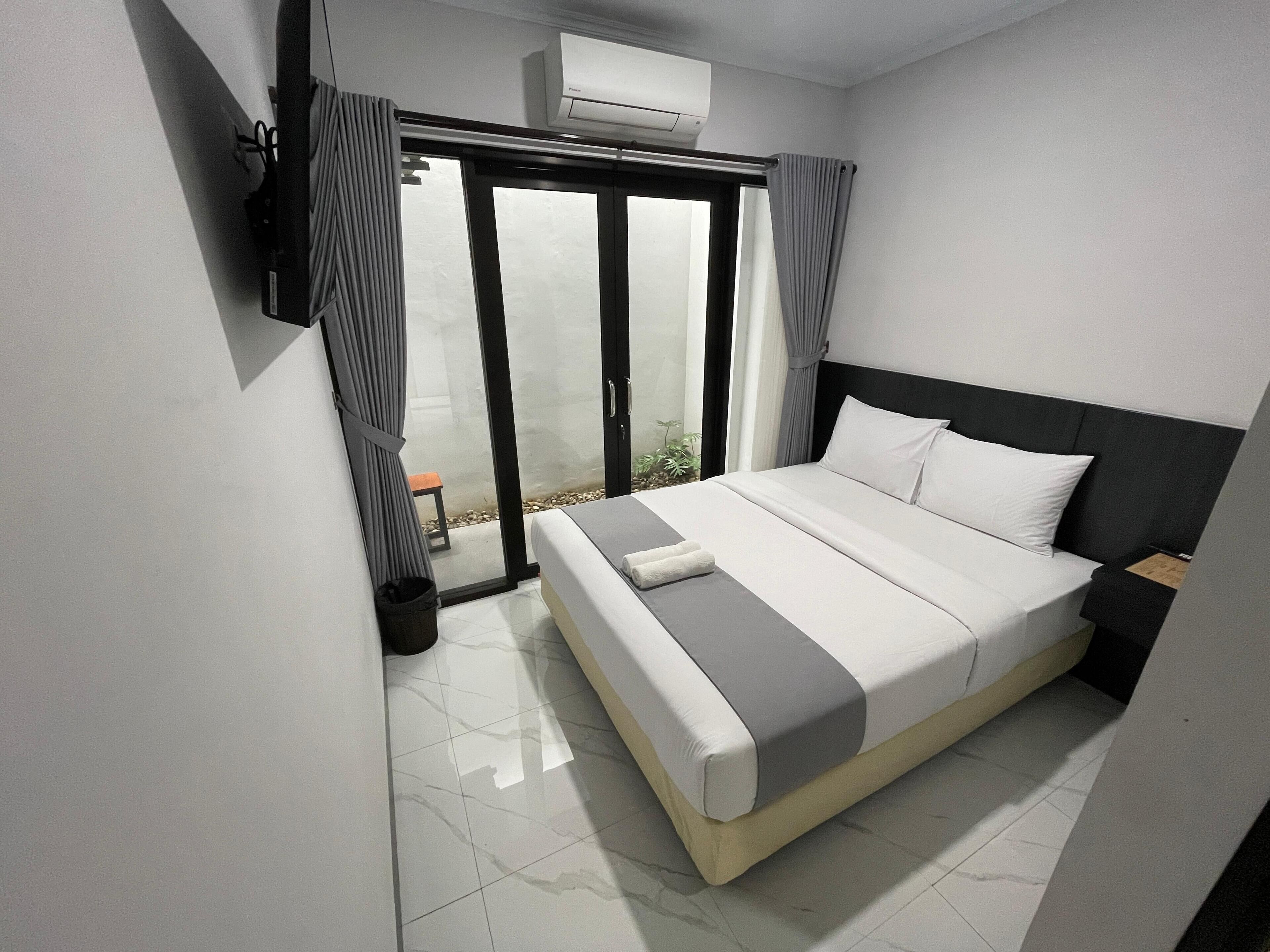 Un dormitorio moderno con cama, puerta corrediza de vidrio que da a un balcón y un equipo de aire acondicionado en la pared.