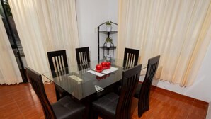Un coin repas avec une table en verre entourée de chaises en bois, une petite étagère avec des plantes et un objet décoratif posé sur la table.