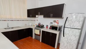 Une cuisine de taille réduite, avec des meubles de couleur sombre, un plan de travail blanc, une cuisinière, un four à micro-ondes et un réfrigérateur.