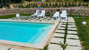 A pool area with a clear blue pool, white lounge chairs, and a colorful umbrella. - House with pool in the open countryside - At Aunt Daniela's House, Oasis in Silence. (Polesio)