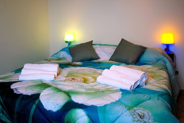 A neatly made bed with a floral comforter, two pillows, and rolled towels.