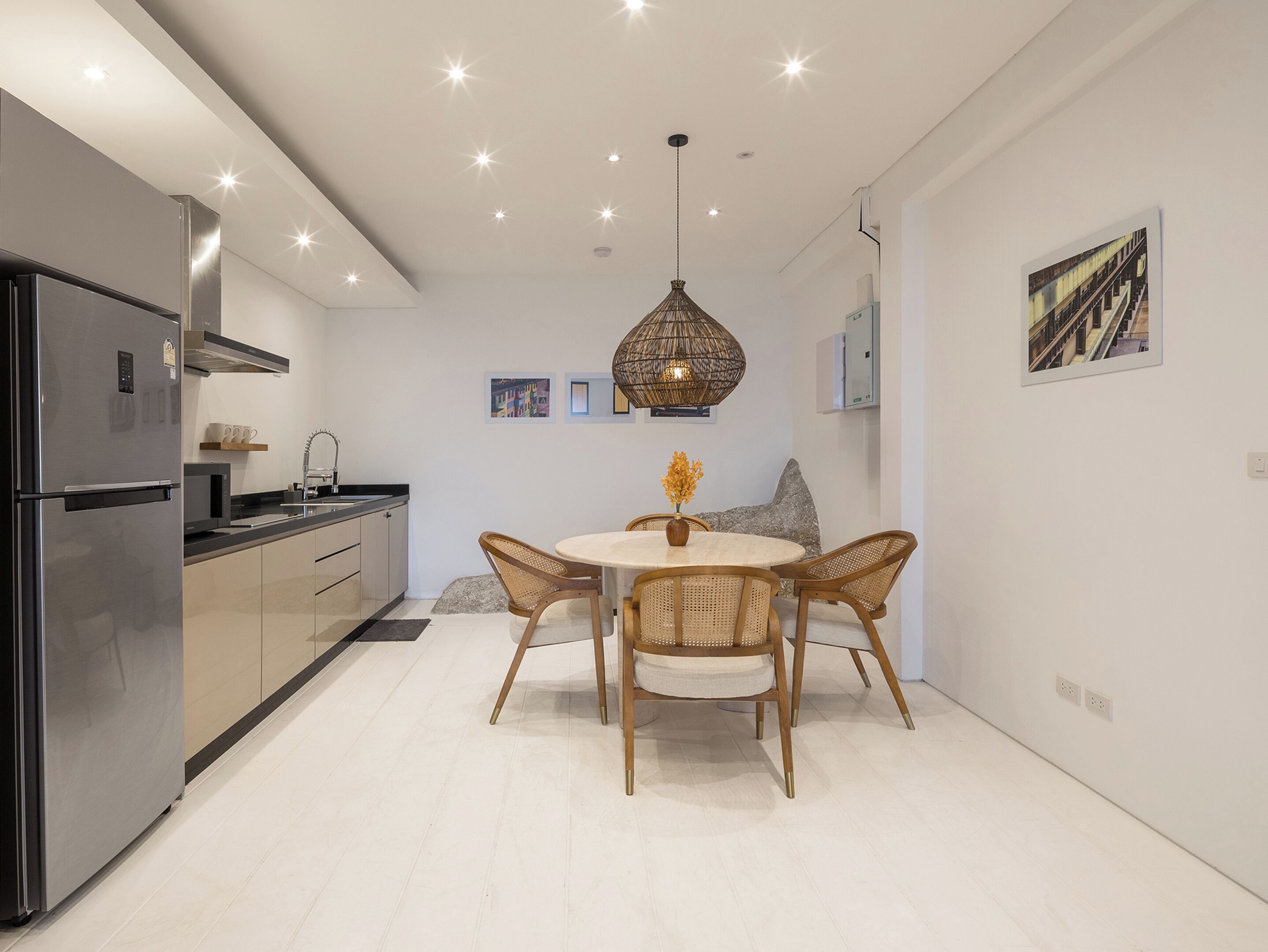 A modern kitchen with a built-in refrigerator, a dining area with a round table and wicker chairs, and a hanging light fixture.