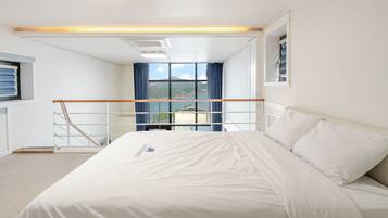 A hotel room with a bed, a window with a view of the outdoors, and a balcony railing.