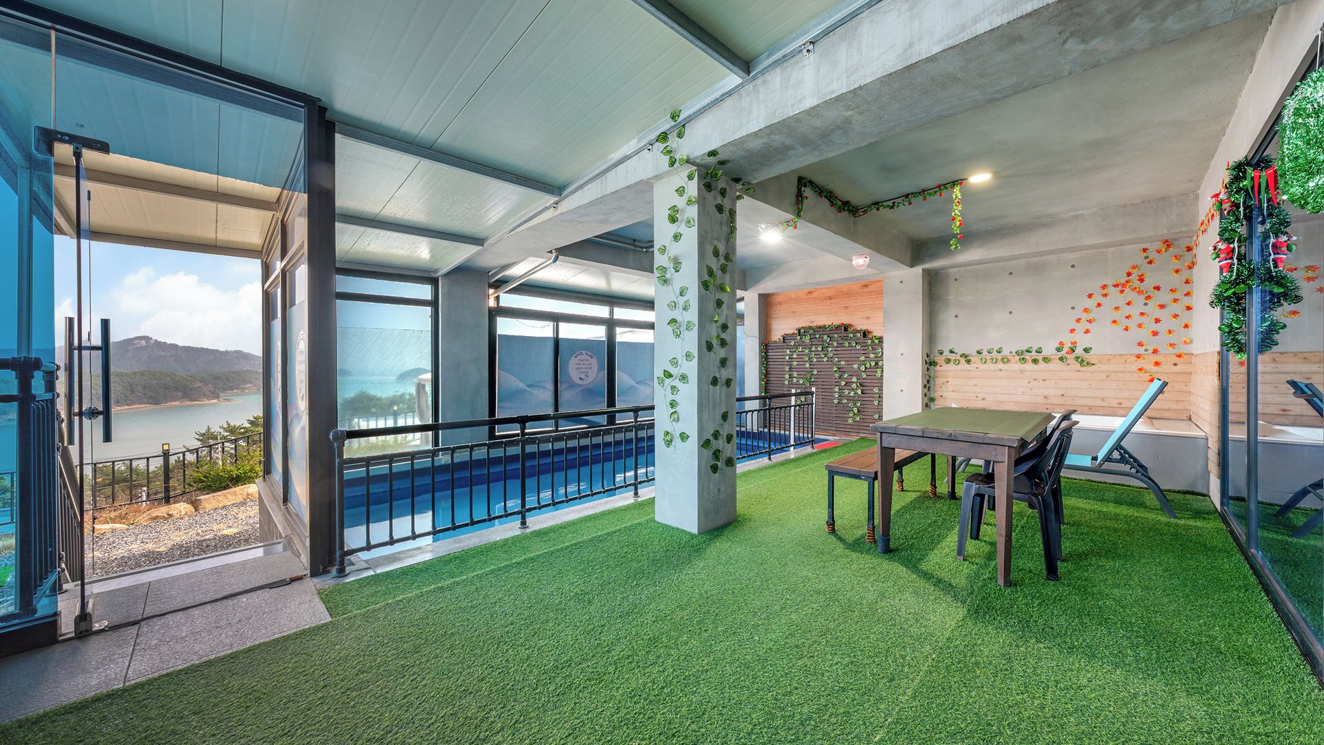 Espaço interno com piscina, grama sintética, mesa e cadeiras, com vista para o mar.