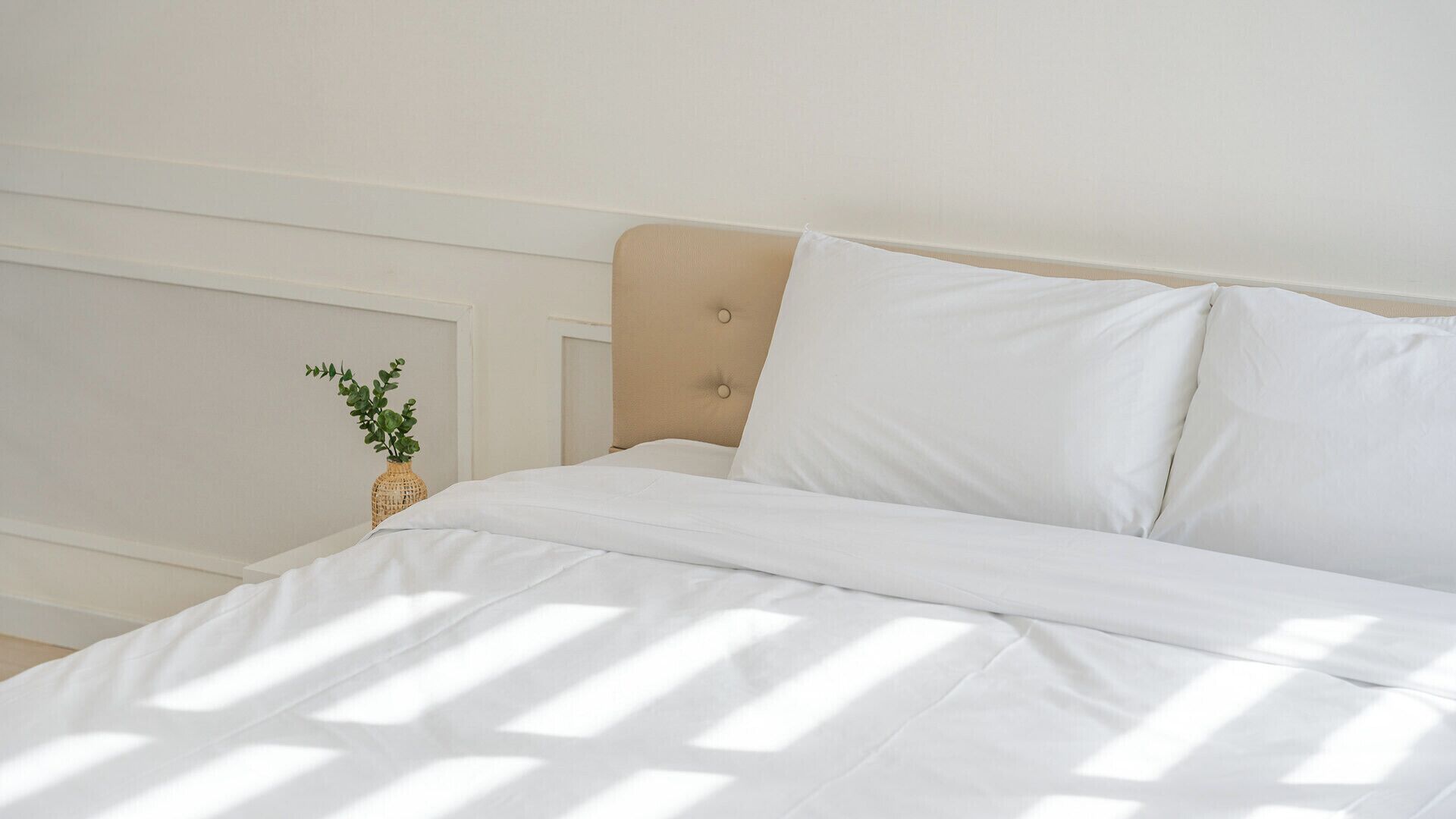 A neatly made bed with white bedding and a beige headboard.