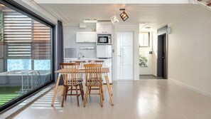 Una cocina moderna con armarios blancos, un microondas y un comedor con sillas y mesa de madera.