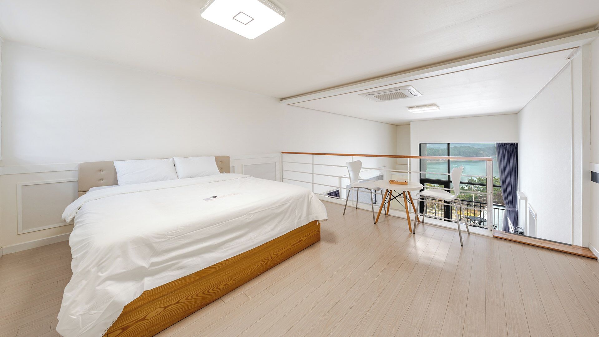 A bedroom with a large bed, a balcony with a view, and a small table with chairs.