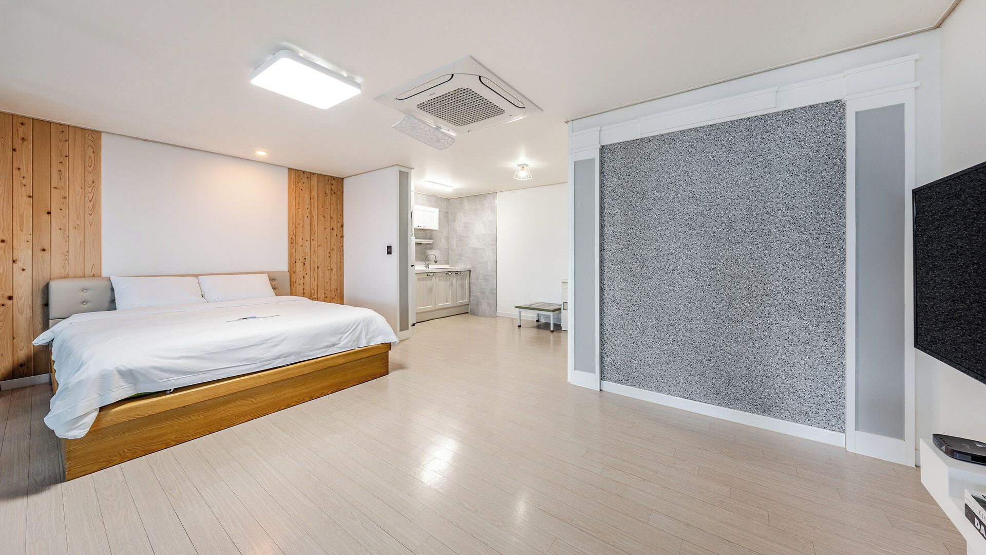 Un dormitorio moderno con una cama, pared de paneles de madera y un separador texturizado gris.