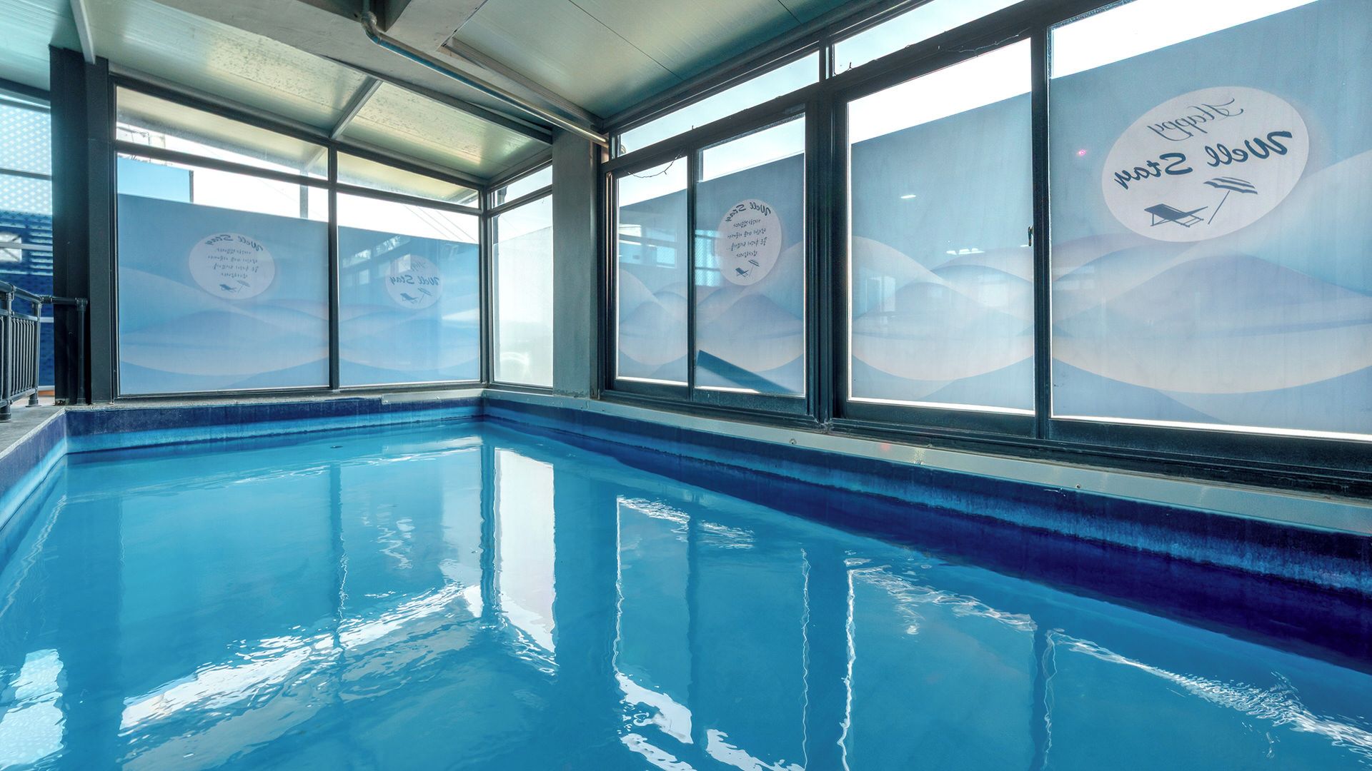 Una piscina interior con paredes de vidrio transparente y borde azul.