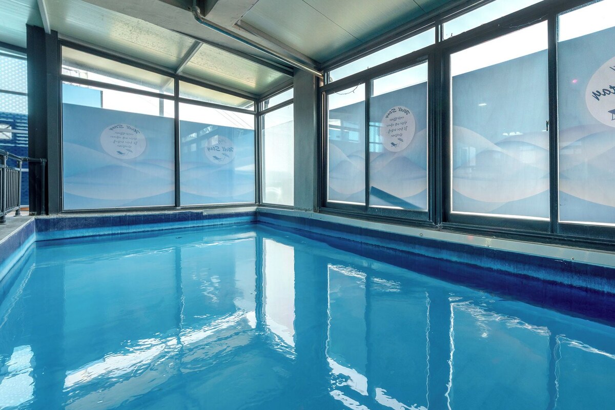 Ein Hallenbad mit klaren Glaswänden und einem blauen Beckenrand.