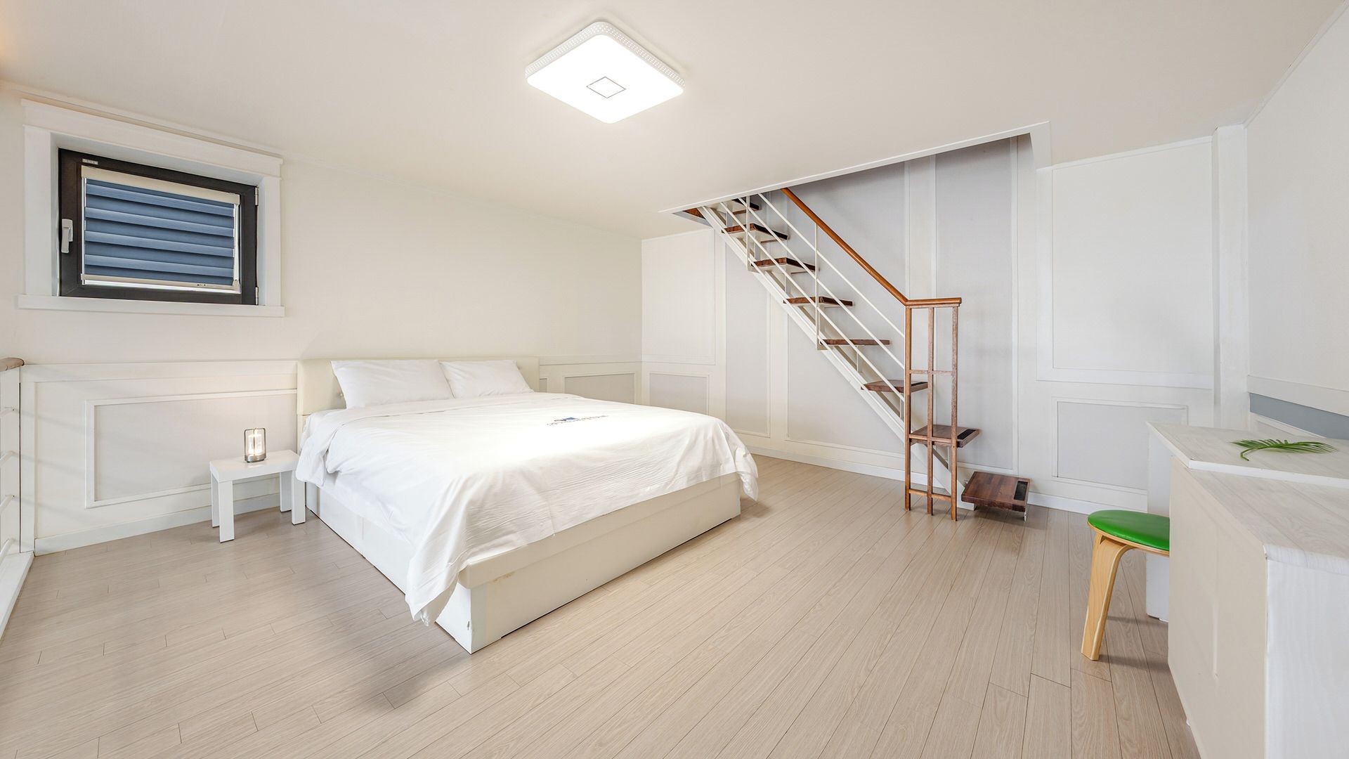 Un dormitorio con cama, mesita de noche, escritorio, silla, escalera y ventana con persianas.