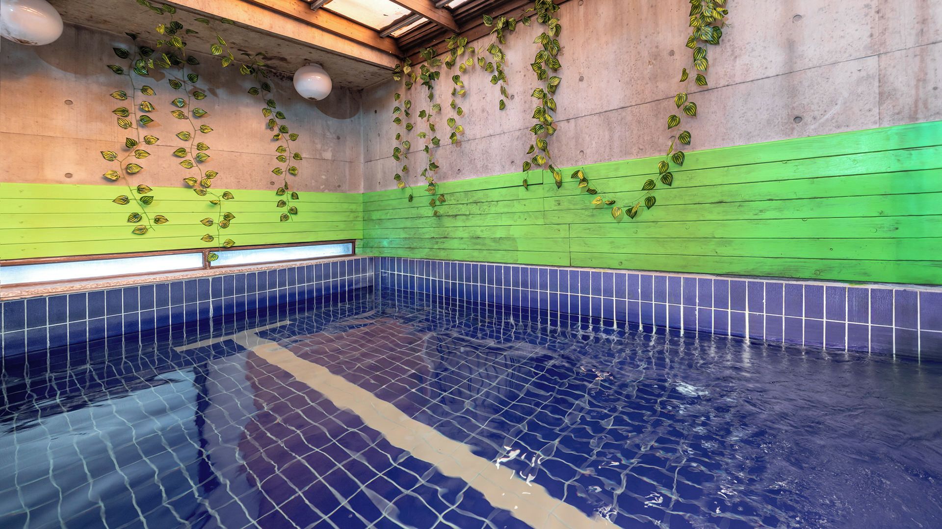 A swimming pool with tiled walls and a tiled floor, surrounded by a green and blue color scheme.