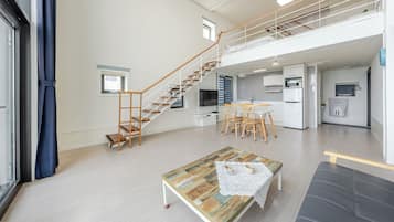 A spacious living area with a staircase, a dining table, and a kitchen in the background.