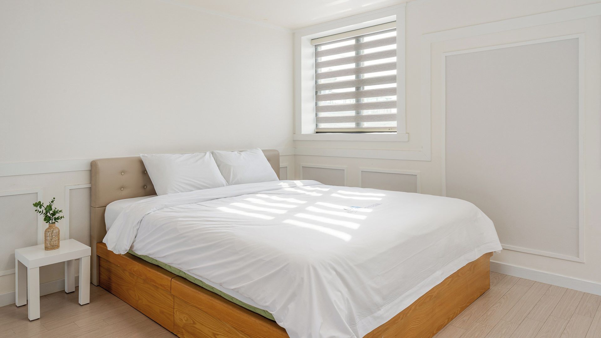 A bedroom with a bed, a nightstand, a window with blinds, and a wall-mounted radiator.
