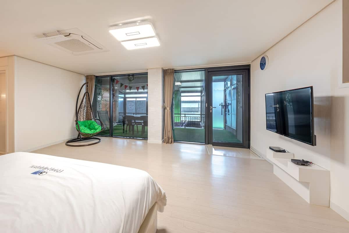 Habitación de hotel con cama, televisión, una silla colgante y puerta corrediza de vidrio que da a un balcón.