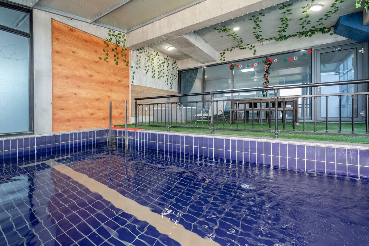 Una piscina interior con azulejos azules, una pared de madera y una puerta de cristal que da a una zona de estar.