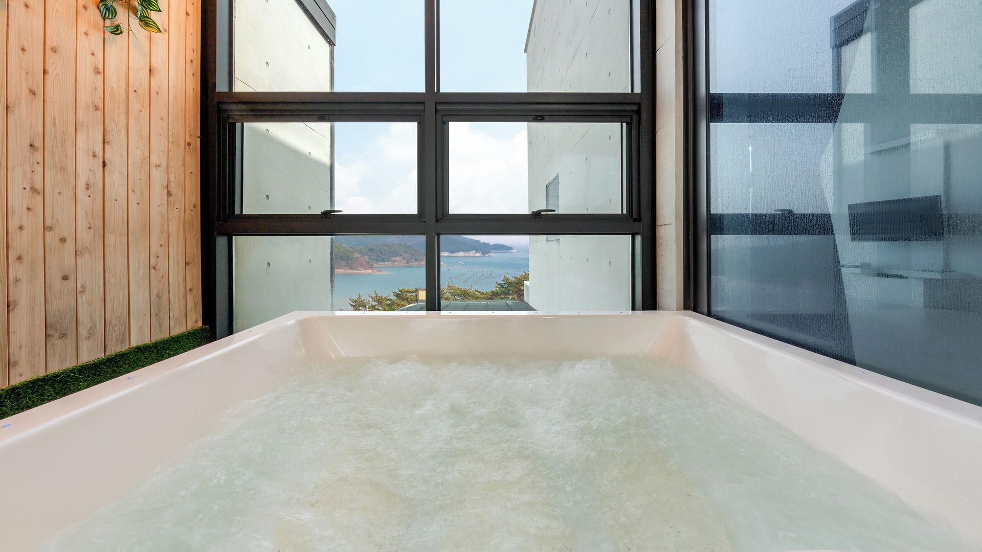 A bathtub with a view of a coastal landscape through large windows.