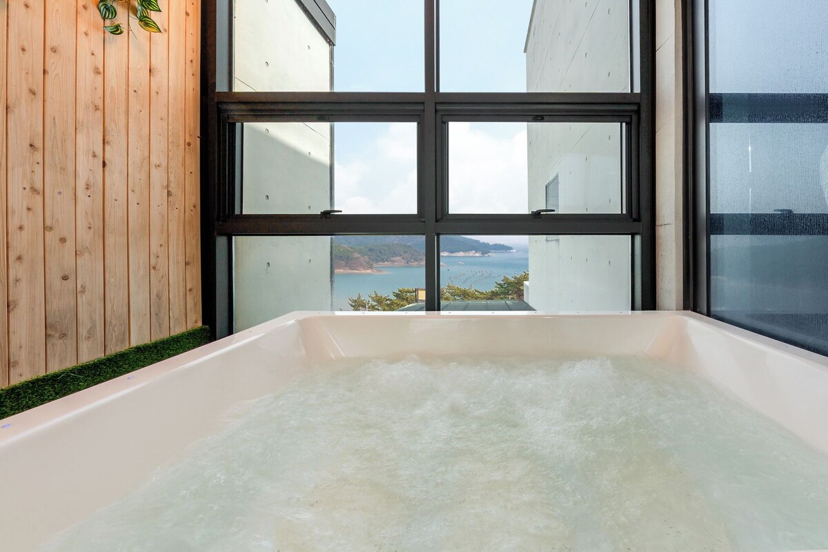Eine Badewanne mit Blick auf eine Küstenlandschaft durch große Fenster.