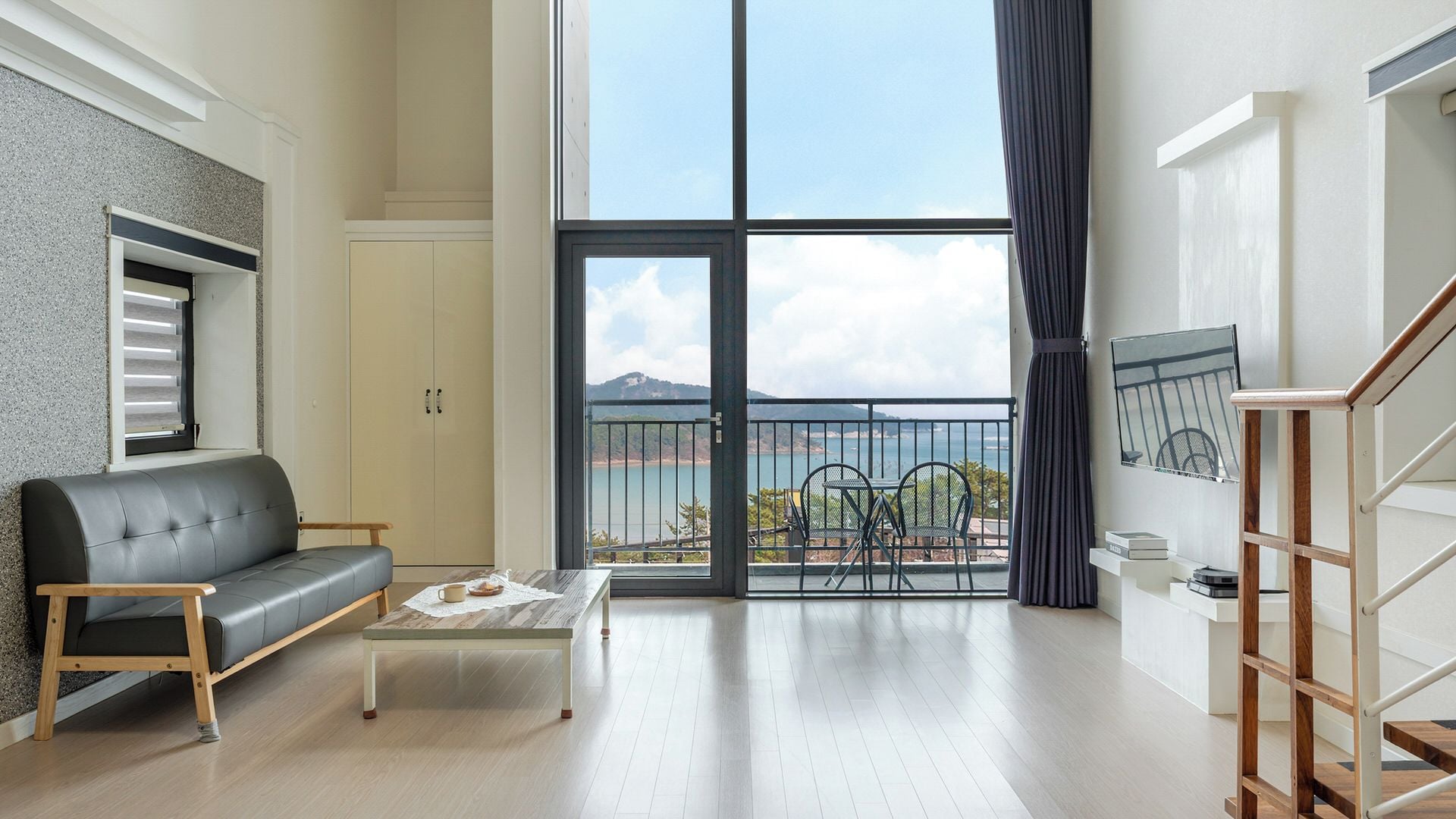 A modern living room with a sofa, coffee table, and a view of the sea through large windows.