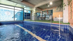 A swimming pool with a tiled edge, a glass enclosure, and a wooden wall with greenery.