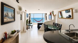A modern kitchen with a glass dining table, a built-in sink, and a view of the sea through large windows.