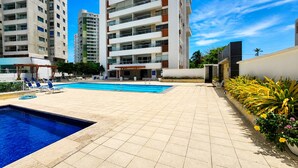 A swimming pool area with tiled flooring, lounge chairs, and a building with multiple balconies in the background. - Ocean view with balcony—pool—Bocagrande Beach—Pet-friendly (Cartagena de Indias)