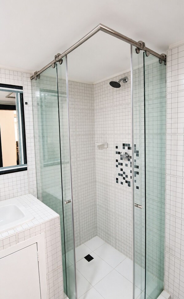 Ein modernes Badezimmer mit einer gläsernen Duschkabine, weißen Fliesen und einem sichtbaren WC.