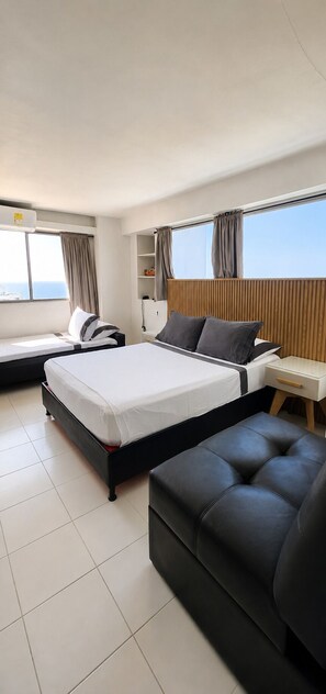 A modern hotel room with a large bed, a sofa, a nightstand, and a view of the sea.