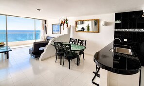 A modern kitchen with a black countertop and a dining area with a glass table and chairs.