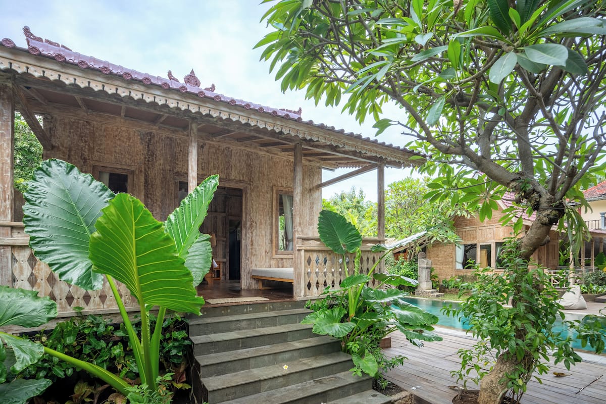 A wooden building with a porch, steps leading to a door, and a pool area.