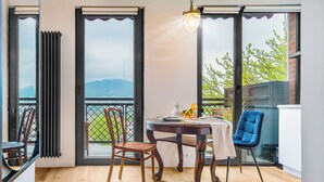 Une pièce comprenant une table à manger, deux chaises, une vue sur la verdure et les montagnes grâce à de grandes fenêtres, et un luminaire suspendu.