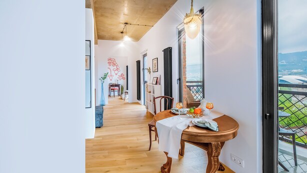 A dining area with a wooden table set for two, a view of the outdoors through a glass door, and a hallway leading to another room. - HB apartments Mikheil Bukhaidze (Tbilisi)