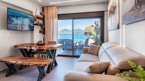 A modern living room with a wooden dining table, a sofa, and a large window with a view of the sea. - Seaside Suite 4 -Modern & Comfort (Episkopos)