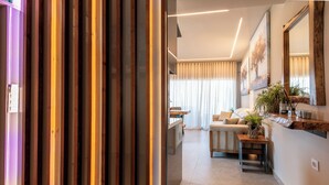 A modern living room with a sofa, a coffee table, and a plant. There is a wooden partition and a large mirror on the wall. - Seaside Suite 4 -Modern & Comfort (Episkopos)