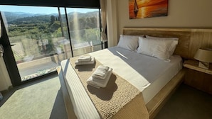 A bedroom with a large bed, a view of the countryside through a sliding glass door, and a painting on the wall. - Seaside Suite 4 -Modern & Comfort (Episkopos)