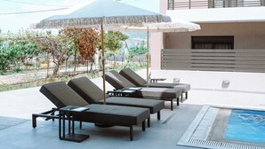 A poolside area with lounge chairs and umbrellas, a pool, and a view of a mountain and vegetation. - Seaside Suite 4 -Modern & Comfort (Episkopos)
