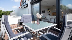 Una terraza con una mesa de vidrio, sillas y un florero con flores.