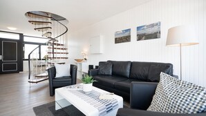 Una sala de estar moderna con una escalera espiral, un sofá de cuero negro, una mesa de centro blanca y una lámpara.