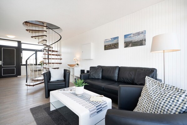 Ein modernes Wohnzimmer mit Wendeltreppe, einem schwarzen Ledersofa, einem weißen Couchtisch und einer Lampe.