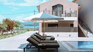 A modern poolside area with lounge chairs and a large umbrella, a staircase leading to a balcony, and a view of the sea and mountains. - Seaside Suite 3-Modern & Comfort (Episkopos)