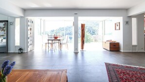 A spacious living room with a large window, a wooden coffee table, and a red patterned rug.