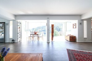 Un salon spacieux avec une grande fenêtre, une table basse en bois et un tapis rouge à motifs.