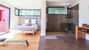A modern bedroom with a large bed, a treadmill, and a glass-enclosed shower area.