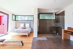 Une chambre moderne dotée d’un grand lit, d’un tapis de course et d’une douche séparée par des parois en verre.
