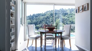 A modern room with a large window, a round table with chairs, and a bookshelf.